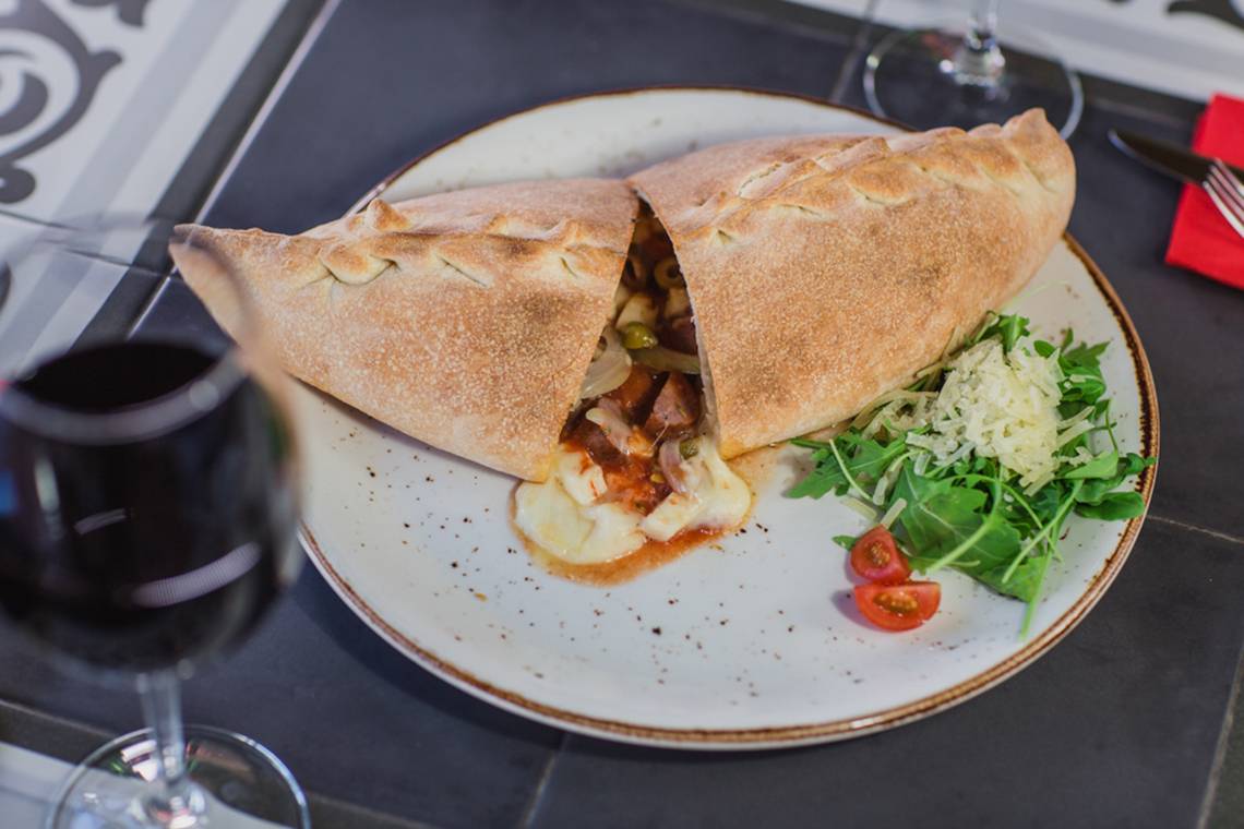 Eine geöffnete Pizza auf einem Teller mit Salat und Tomaten neben einem Glas Rotwein.