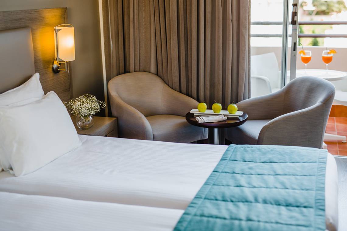 Hotelzimmer im Napa Plaza mit zwei Betten, Sesseln, Tisch und Aussicht auf einen Balkon.