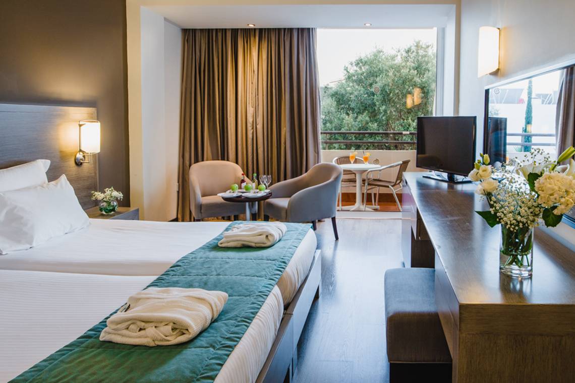 Innenansicht eines Doppelzimmers im Napa Plaza Hotel mit zwei Betten, einem kleinen Tisch, einem Fernseher und einer Aussicht auf den Balkon.