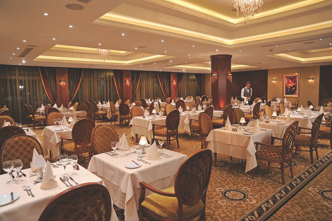 Alexander The Great Hotel Restaurant mit gedeckten Tischen und einem Kellner.