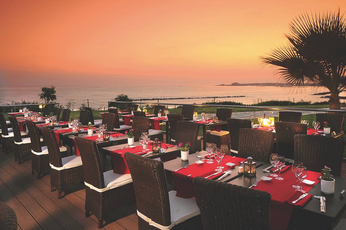 Alexander The Great Hotel Terrasse mit eingerichteten Tischen und Blick auf den Ozean bei Sonnenuntergang