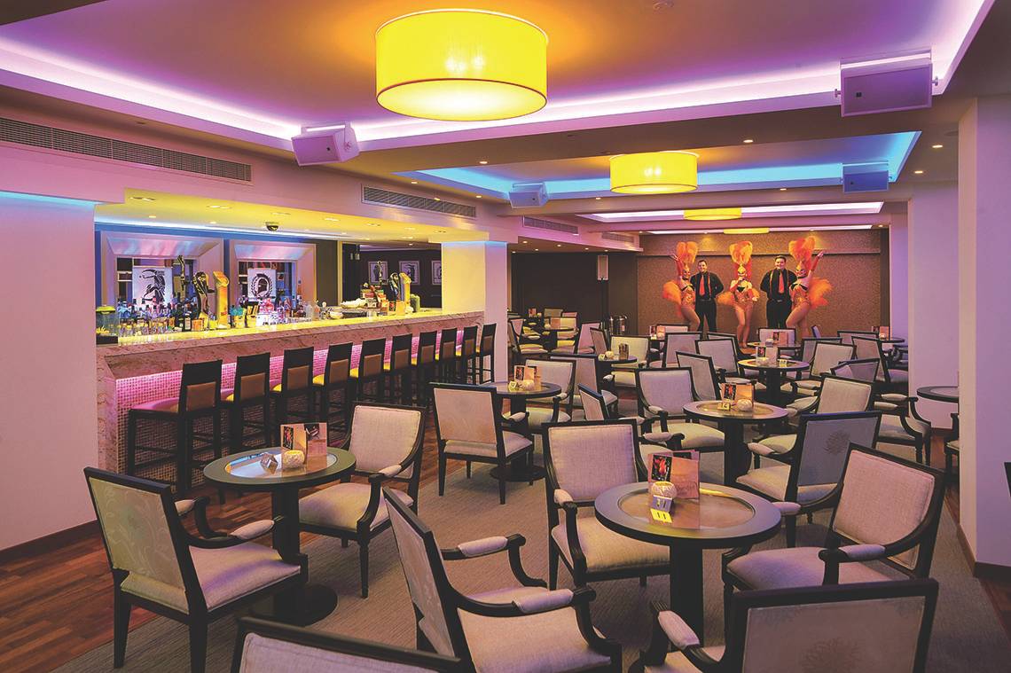 Cocktailbar im Alexander The Great Hotel mit farbiger Beleuchtung und Barstühlen.