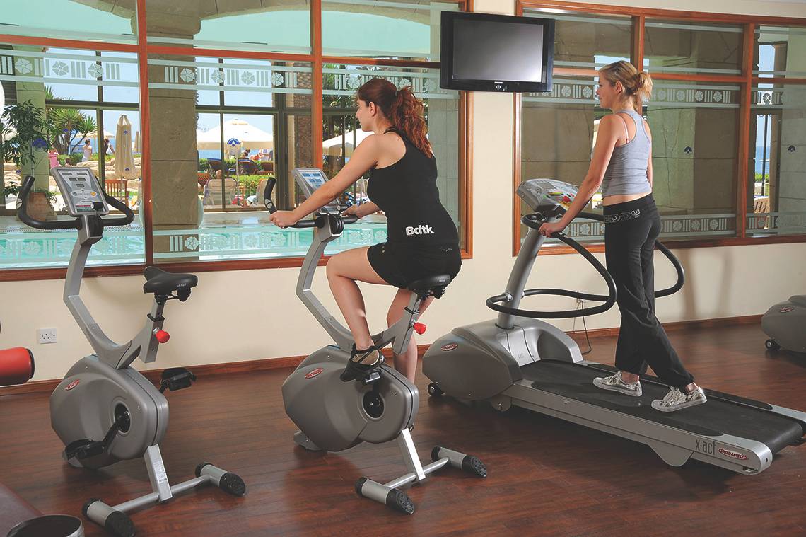 Zwei Frauen trainieren im Fitnesscenter des Alexander The Great Hotels auf einem Laufband und einem Fahrrad.