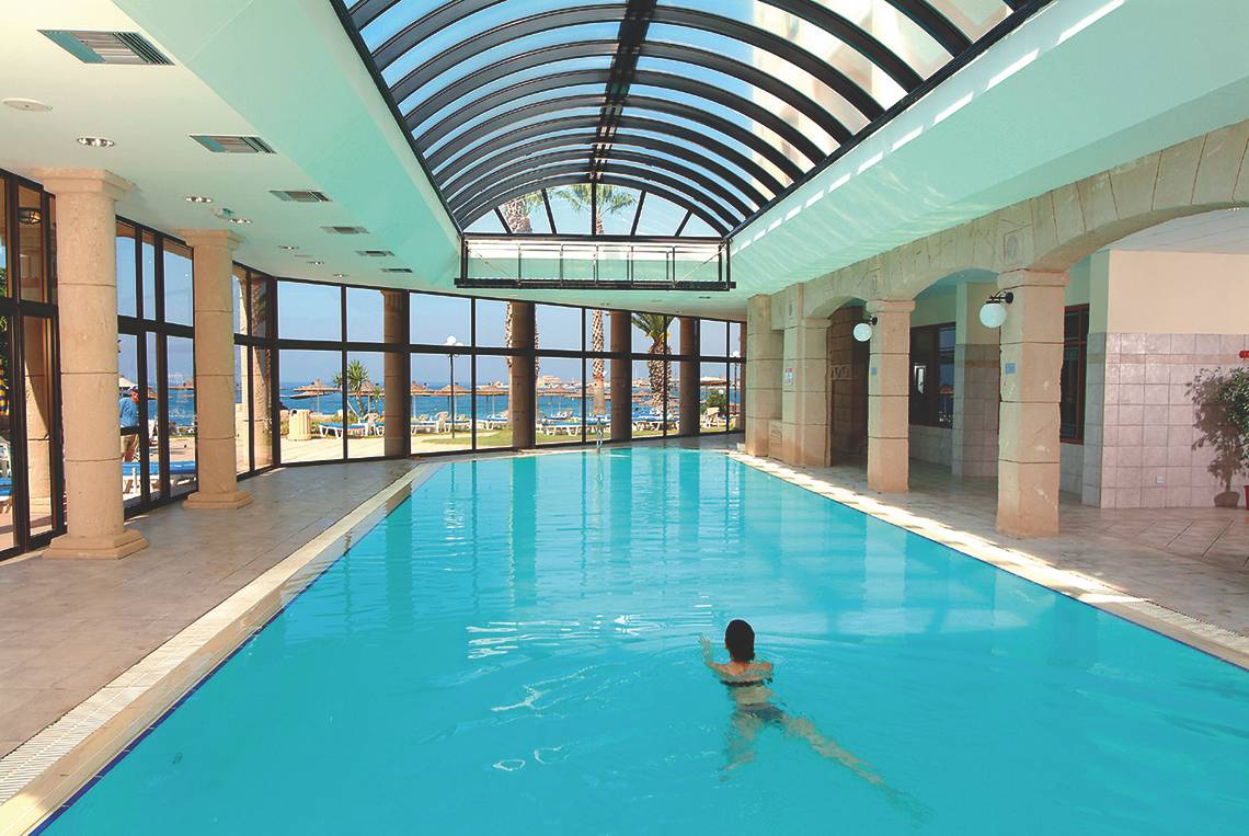 Eine Frau schwimmt im grünen Wasser des Innenpools des Alexander The Great Hotels.