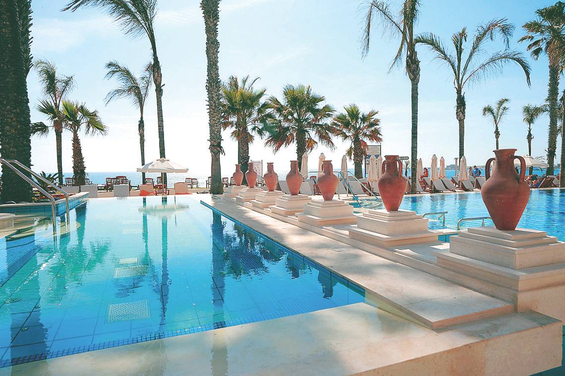 Außenpool des Alexander The Great Hotels mit blauem Wasser und roten Vasen.