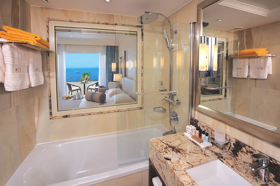 Alexander The Great Hotel Badezimmer mit Badewanne, Spiegel und Meerblick.