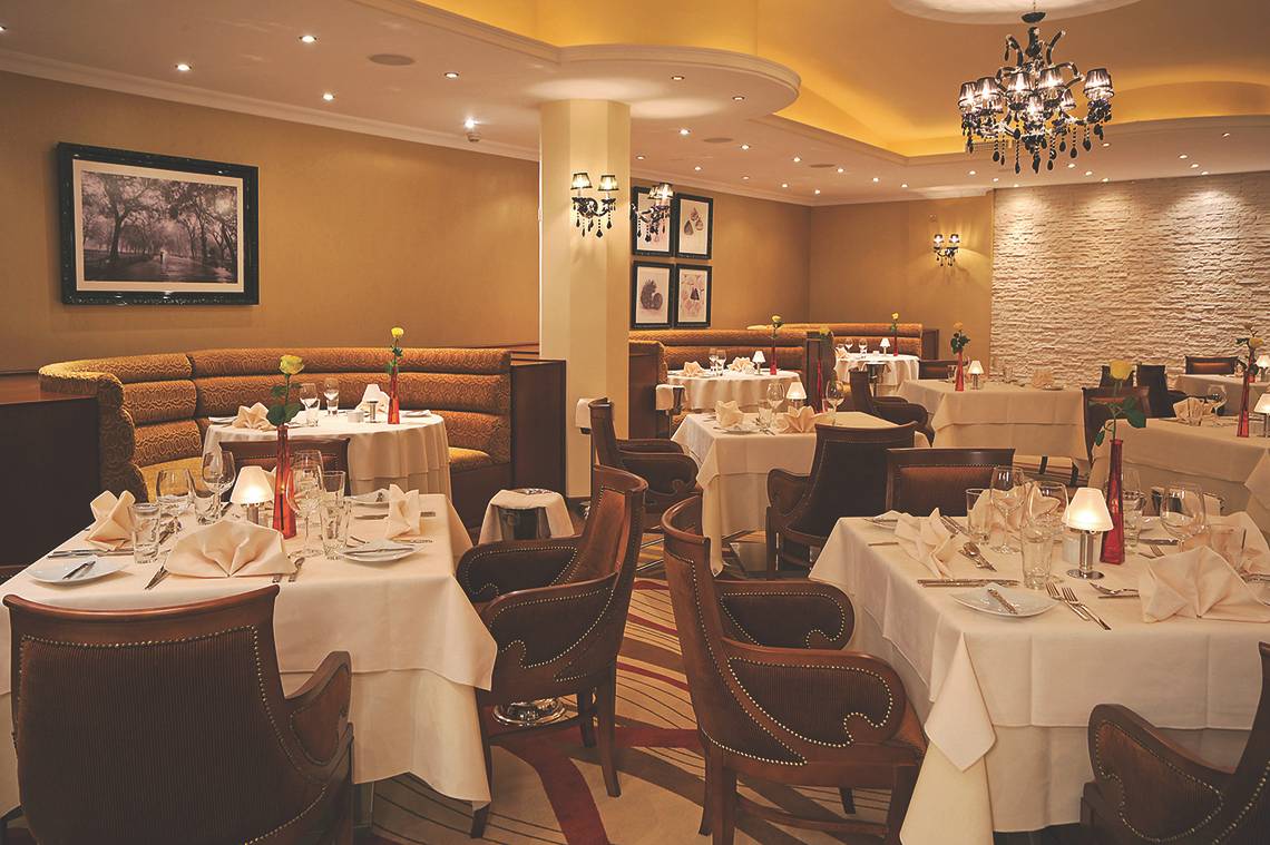 Innenansicht des Alexander The Great Hotels mit geräumigem Restaurant und elegant eingerichteten Tischen.