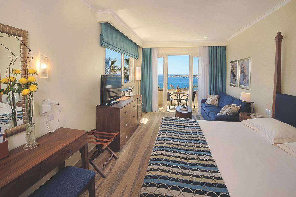Zimmer im Alexander The Great Hotel mit Meerblick, Fernseher, Sofa und Balkon.