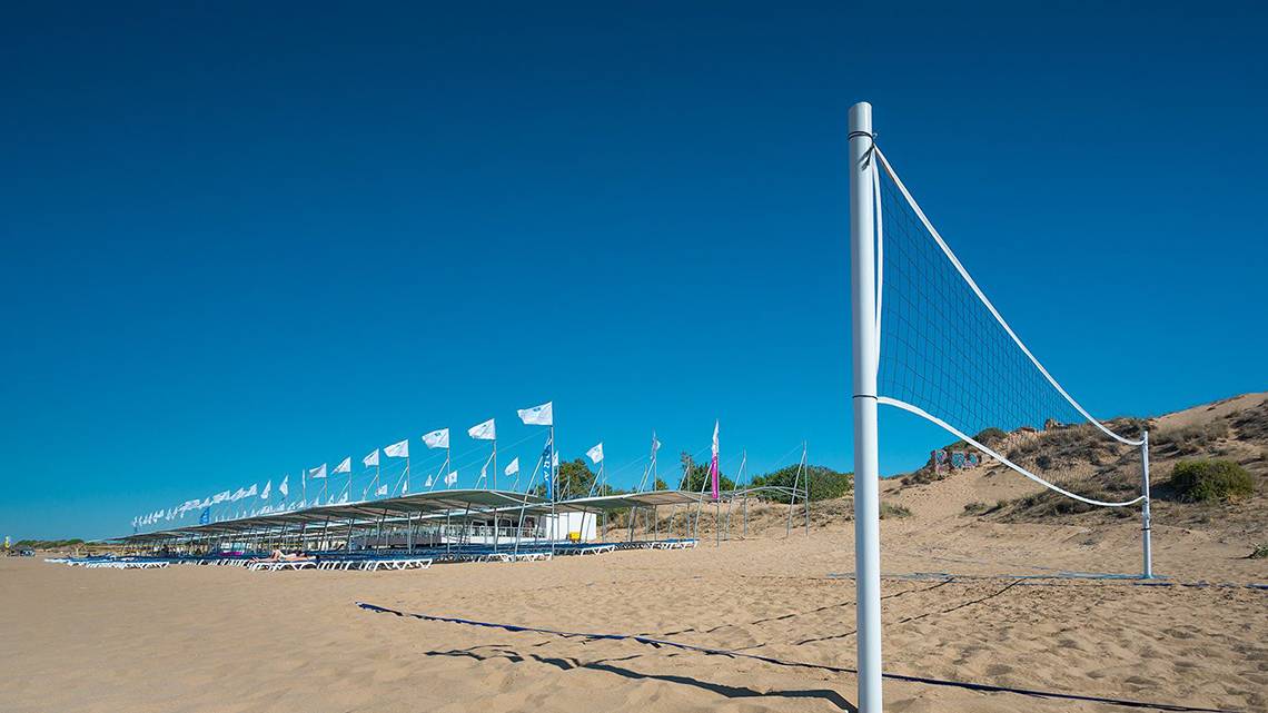 Ein Volleyballnetz auf dem Strand des Terrace Elite Resorts mit vielen Sonnenliegen und Fahnen im Hintergrund.
