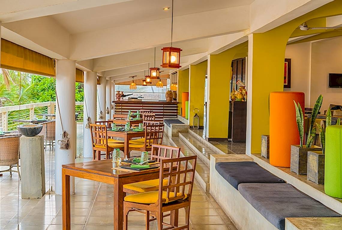 Innenansicht des Restaurants Jetwing Sea mit holzigen Tischen und Stühlen, gelben Wänden und Pflanzen.
