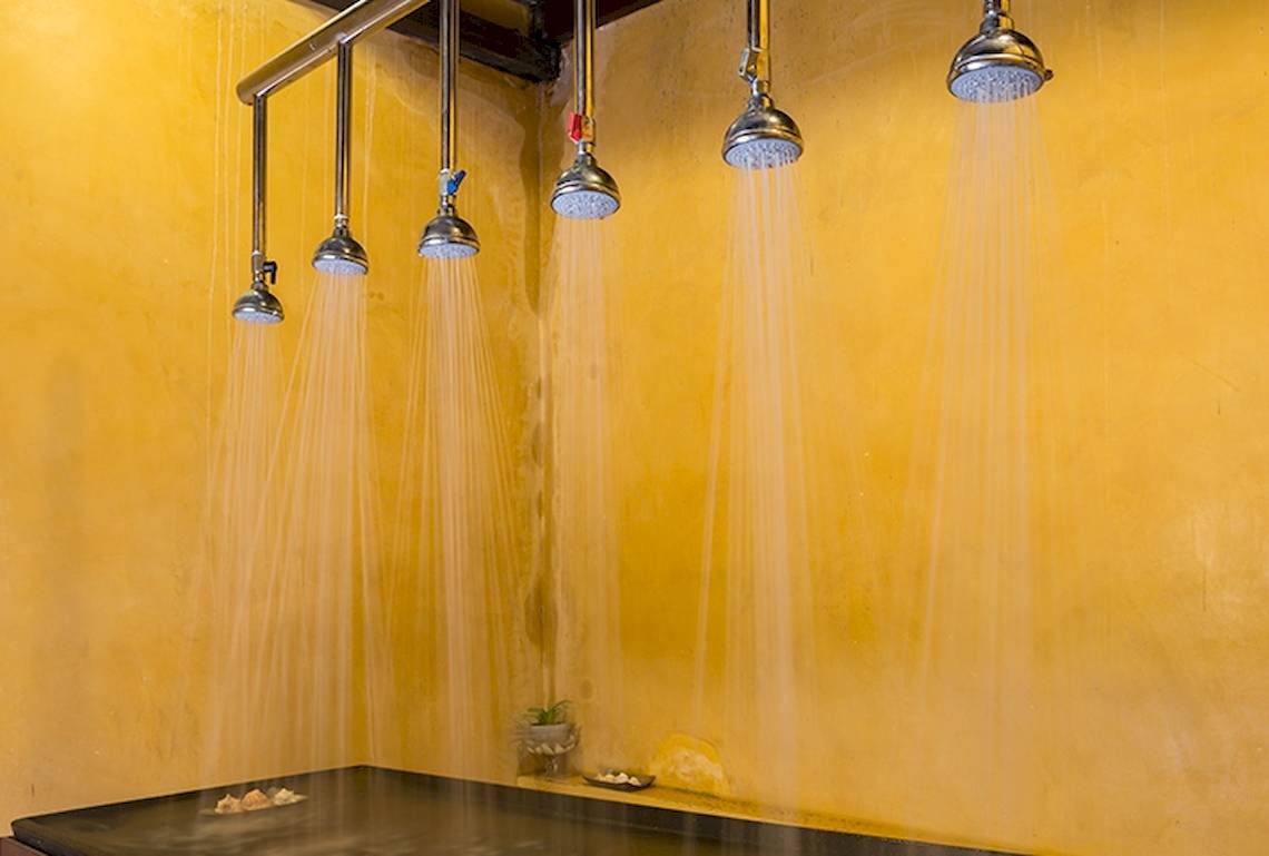 Ein Raum mit mehreren Duschköpfen, die Wasser sprühen, an einer gelben Wand.