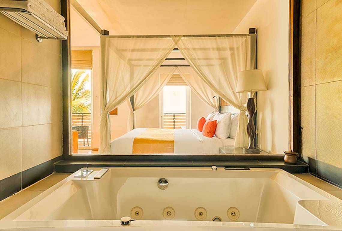 Badezimmer des Jetwing Sea Hotels mit Badewanne und Blick auf ein Bett mit Baldachin.