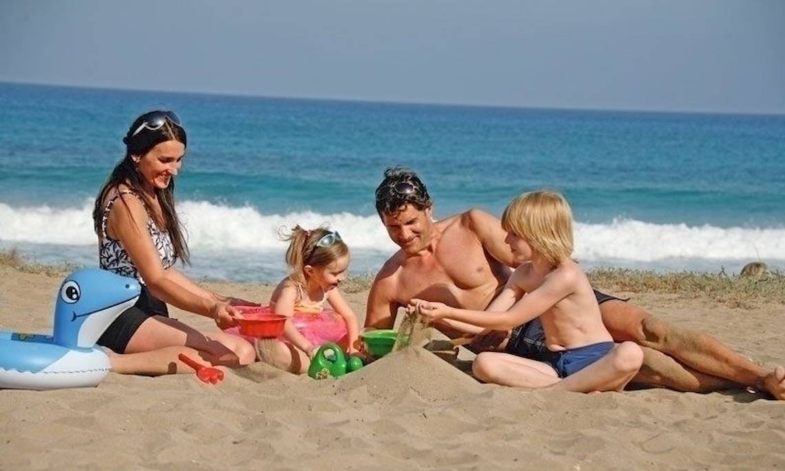 Eine Familie am Strand mit Kindern und Meer im Hintergrund.