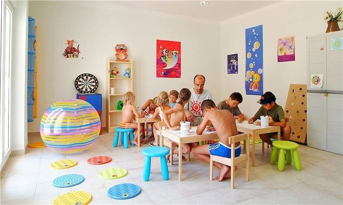 Gruppe von Kindern und einem Mann, die an Tischen in einem Raum im Universal Hotel Aquamarin sitzen.