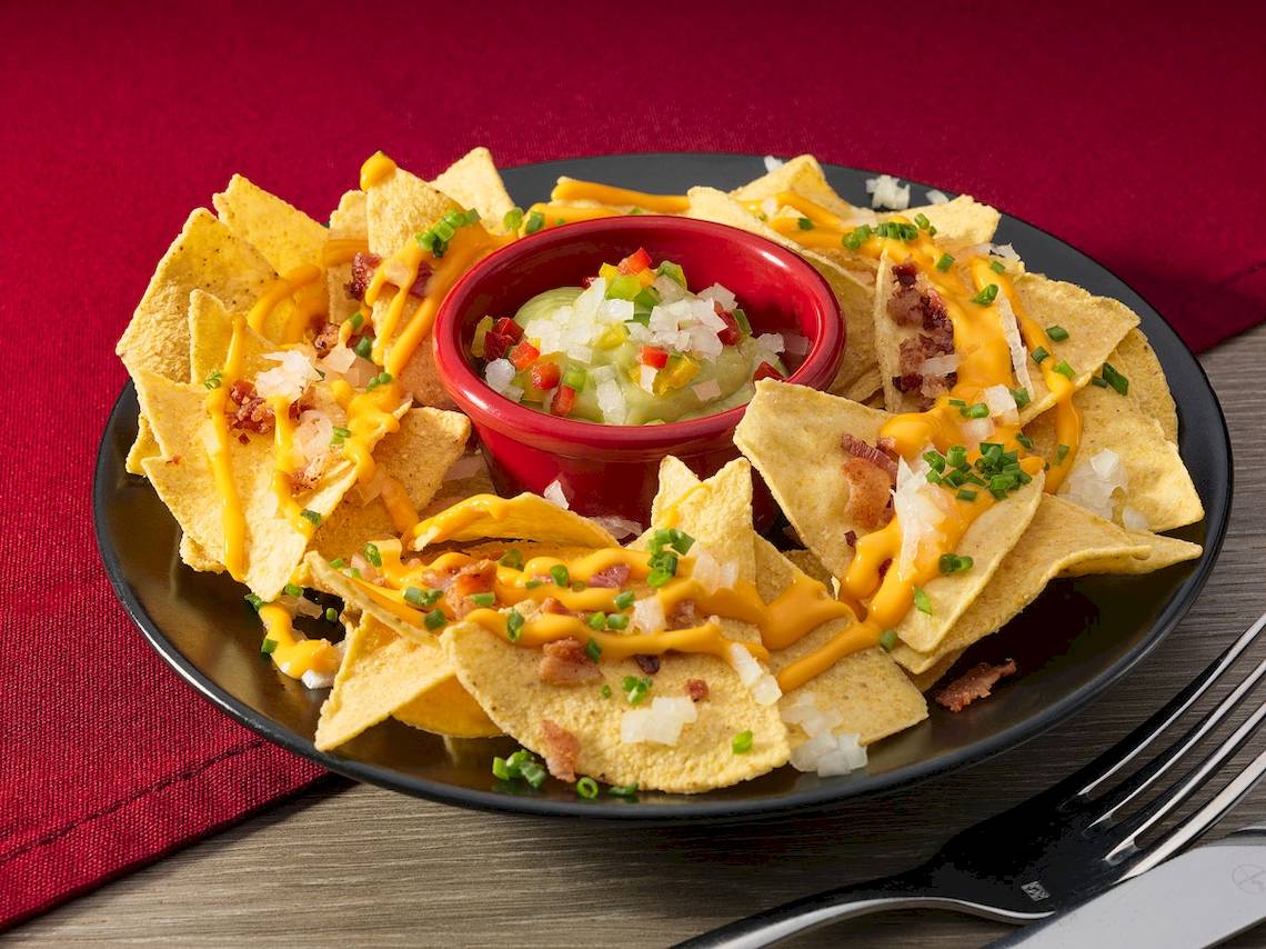 Ein Teller mit Nachos, überzogen mit Käse, Speck und Salsa, auf einem Tisch.