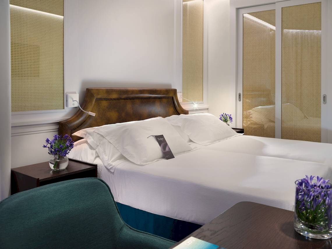 Doppelbett-Zimmer im H10 Conquistador Hotel mit weißen Laken, Kissen und Blumenvasen.