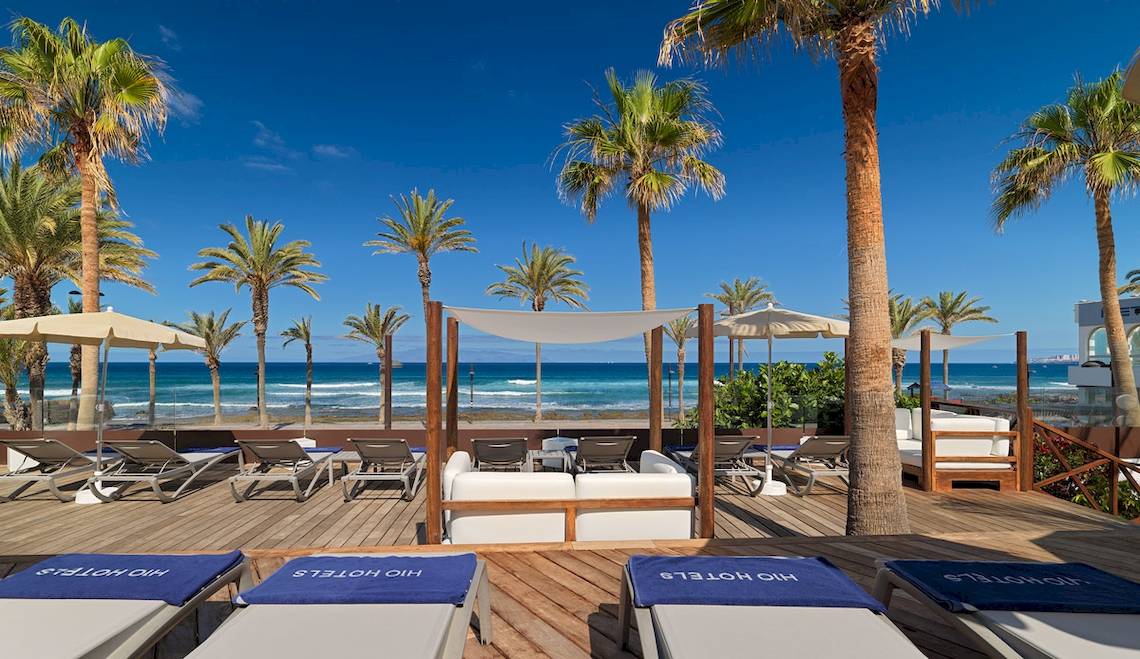Außenterrasse des H10 Conquistador Hotels mit Lounge-Liegestühlen, Sonnenschirmen und Meerblick.