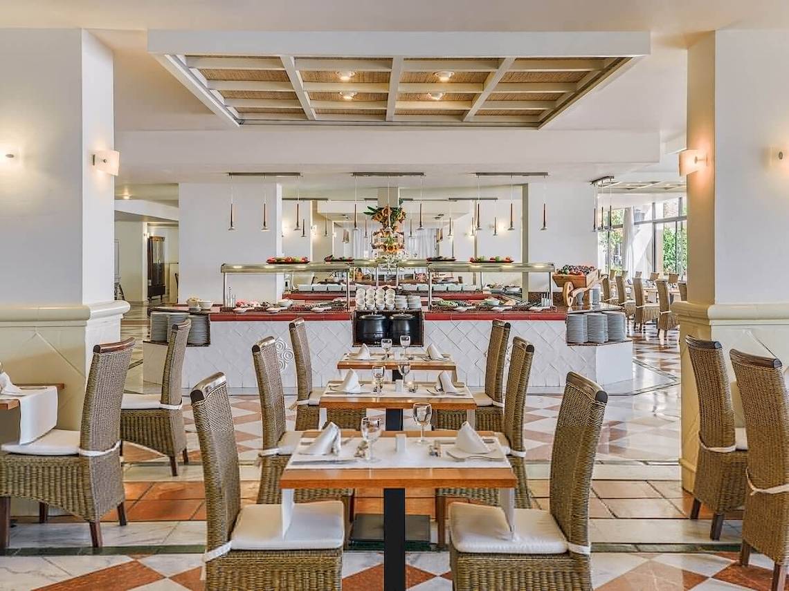 Innenansicht des Restaurants im H10 Conquistador Hotel mit Tisch, Stühlen und Buffet.