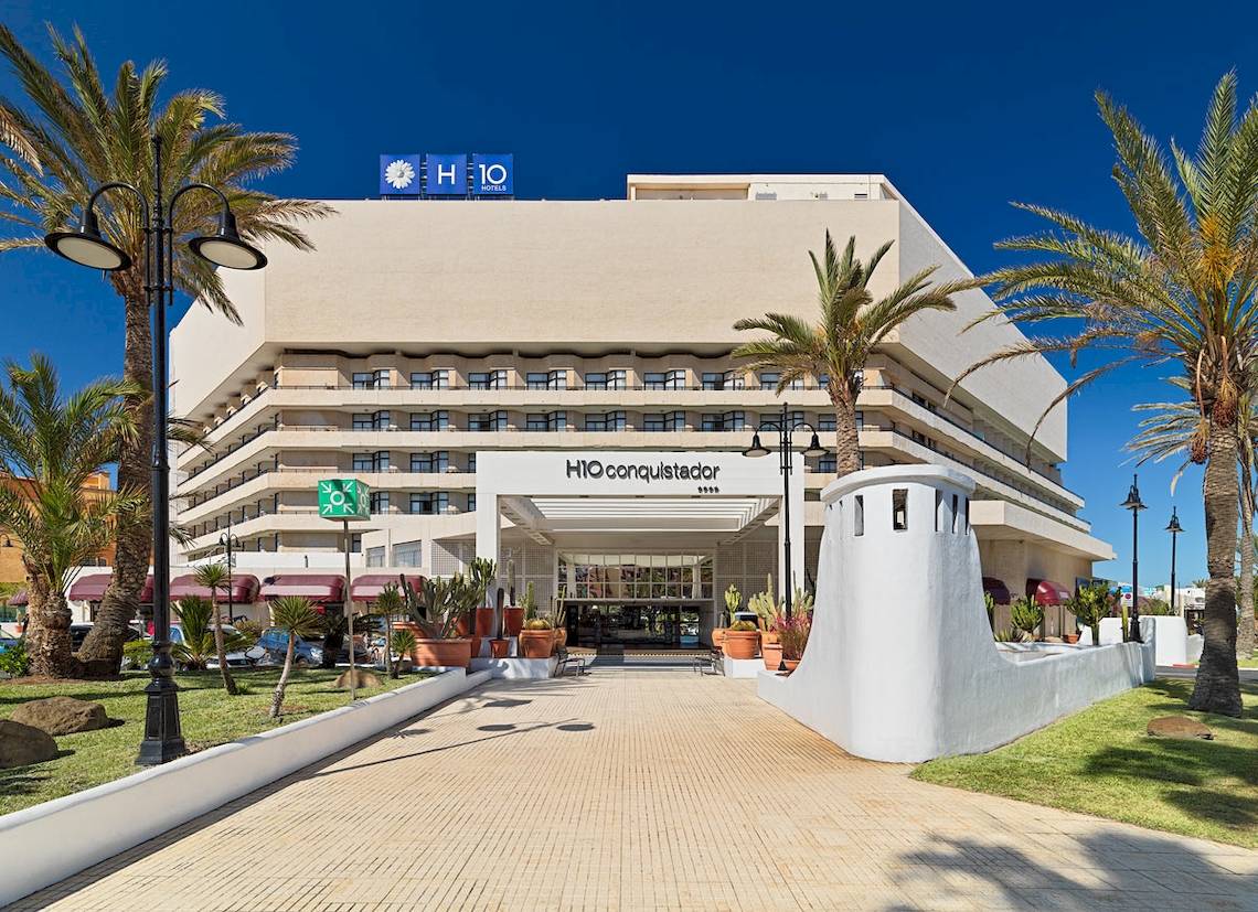 Das H10 Conquistador Hotel mit vielen Palmen und Pflanzen vor dem Eingang.