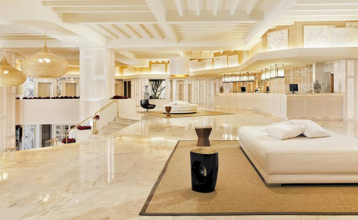 Lobby des H10 Conquistador Hotels mit Marmorboden, weißen Möbeln und hohen Decken.