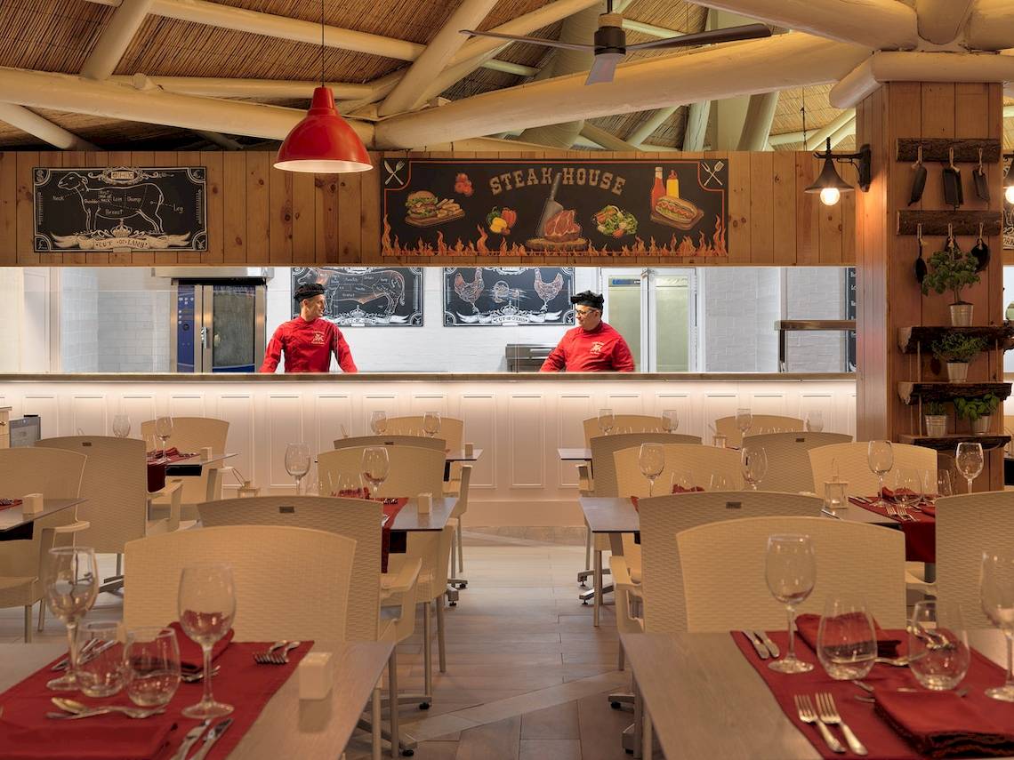 Innenansicht der Steakhouse im H10 Conquistador Hotel mit Angestellten am Tresen und leeren Tischen.