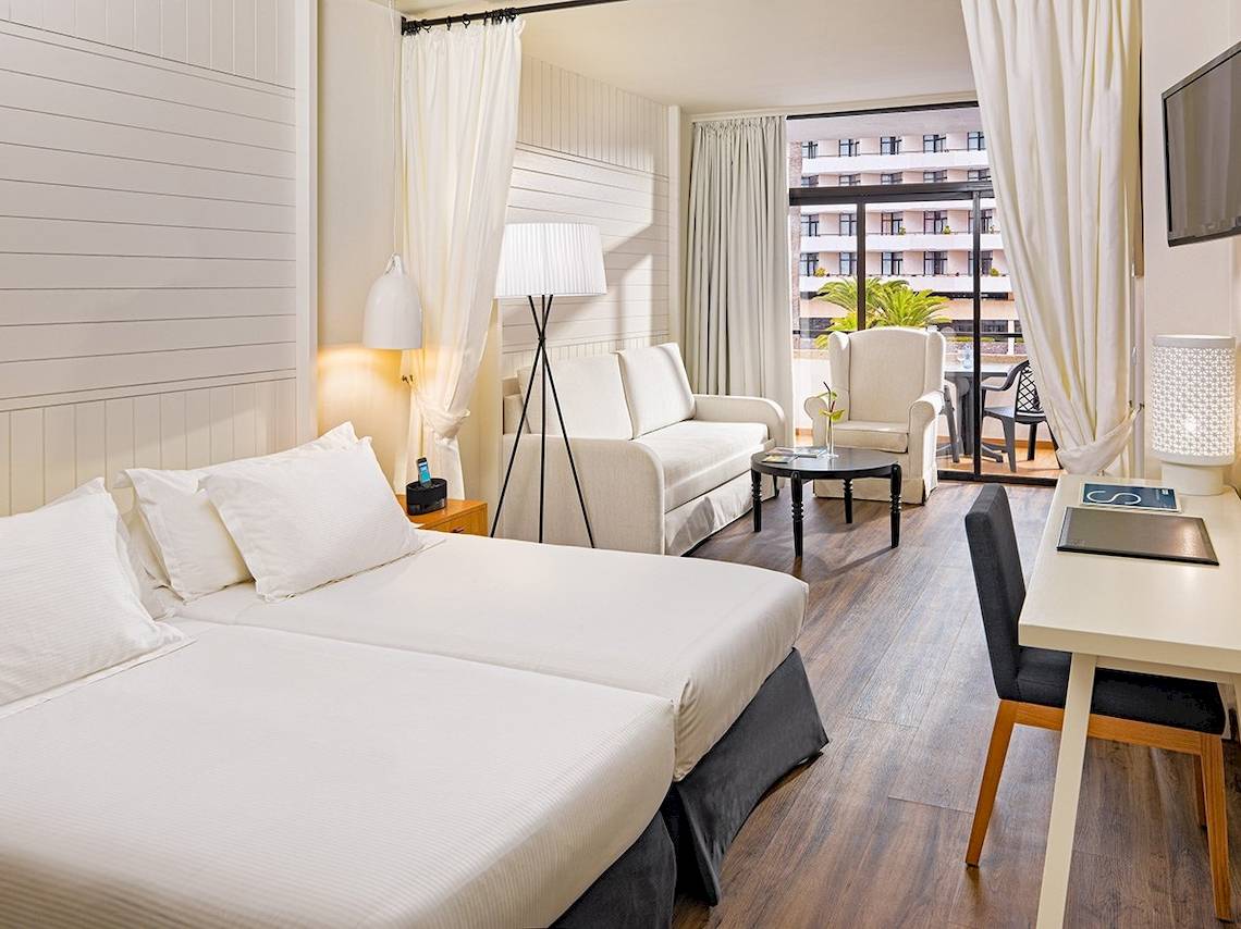 Innenansicht eines Doppelzimmers im H10 Conquistador Hotel mit zwei Betten, Schreibtisch und Balkon.