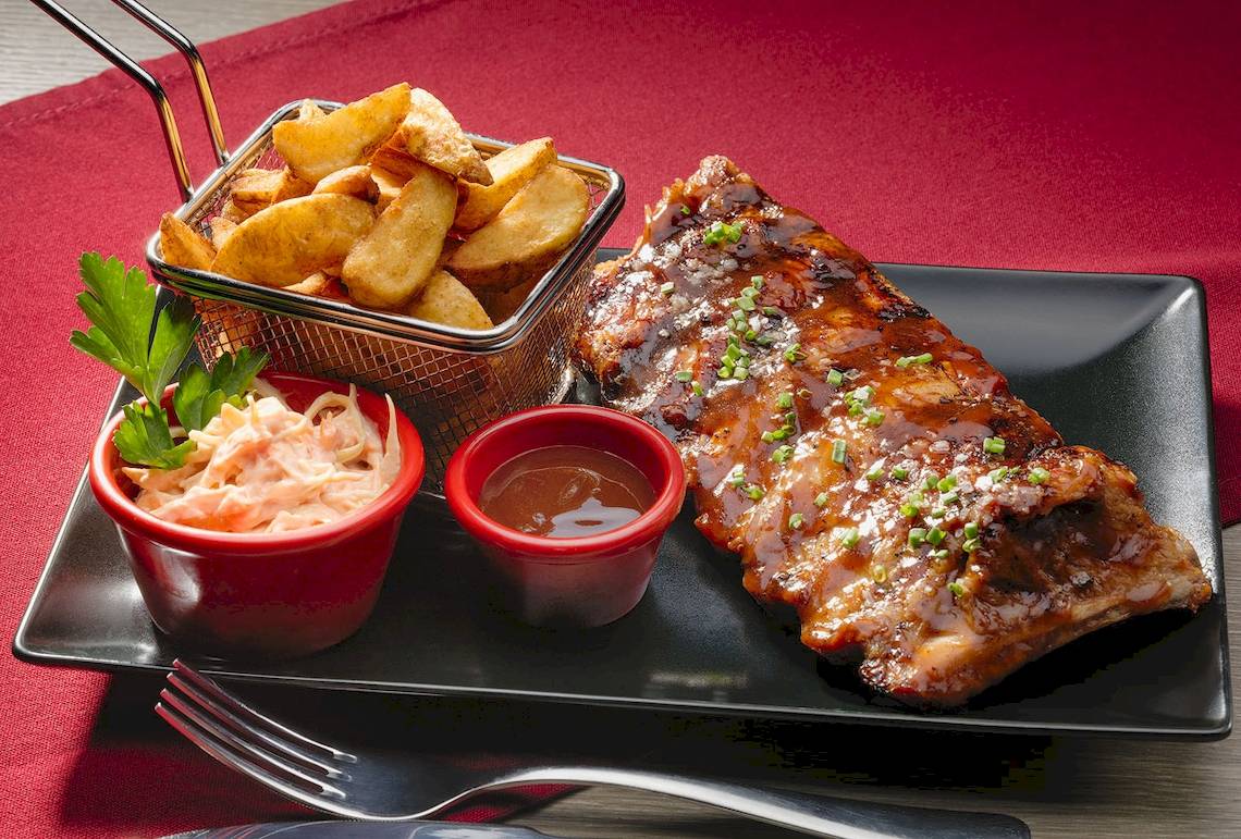 Gegrillte Rippchen mit Beilagen auf schwarzem Teller