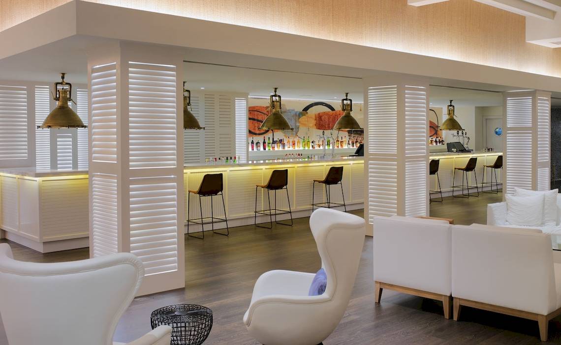 Lobby Bar des H10 Conquistador Hotels mit weißen Möbeln und Theke.