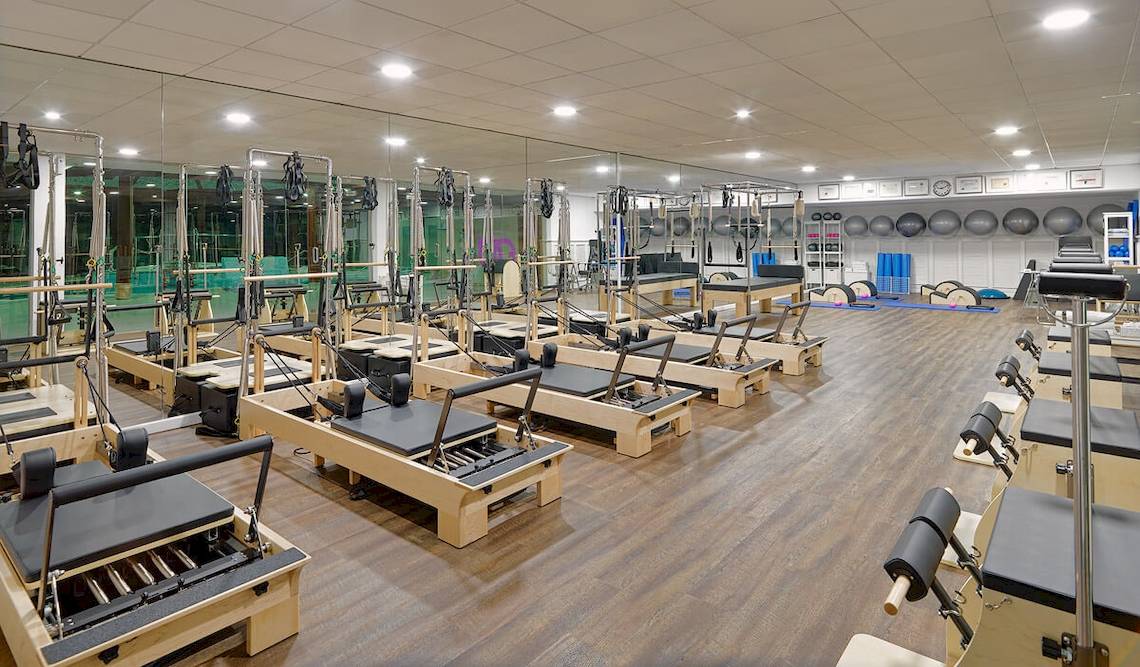 Fitnessstudio mit Pilates Reformer Geräten, großen Spiegeln und Holzboden.