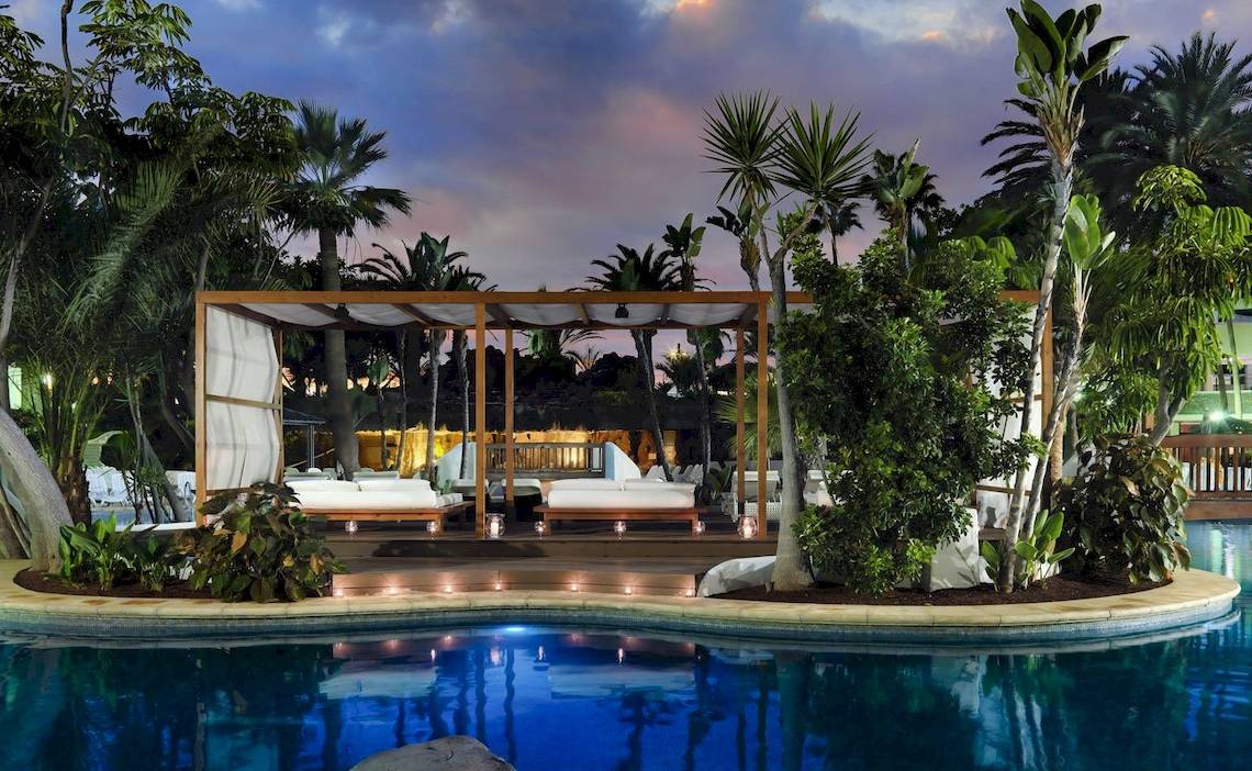 Loungebereich am Pool des H10 Conquistador Hotels mit überdachter Terrasse und beleuchteten Betten.