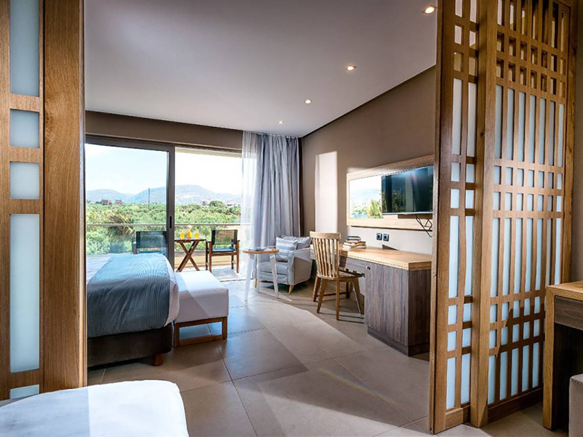 Innenansicht eines Hotelzimmers im Stella Palace Resort & Spa mit Bett, Schreibtisch, Fernseher und Terrassenblick.