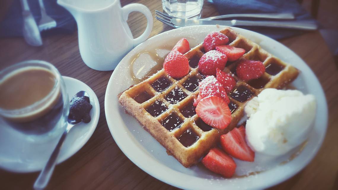 Ein Teller mit einer Waffel, Erdbeeren, Sahne und Kaffee.