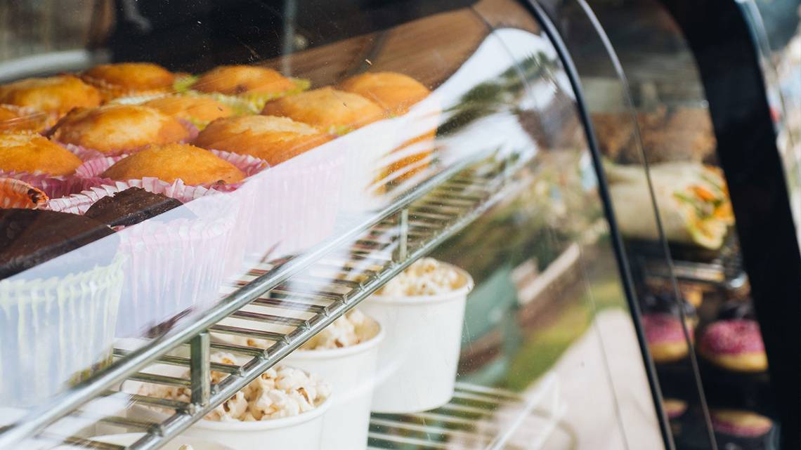 Eine Vitrine mit verschiedenen gebackenen Gütern, einschließlich Muffins, Popcorn und Schokolade, in einer Bäckerei.