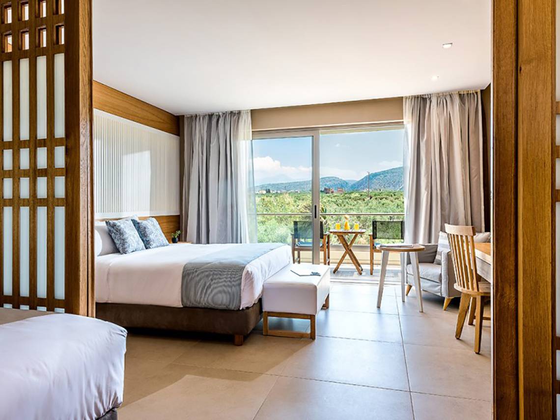 Innenansicht eines Zimmers im Stella Palace Resort & Spa mit zwei Betten, Tisch, Stühlen und einem Balkon.