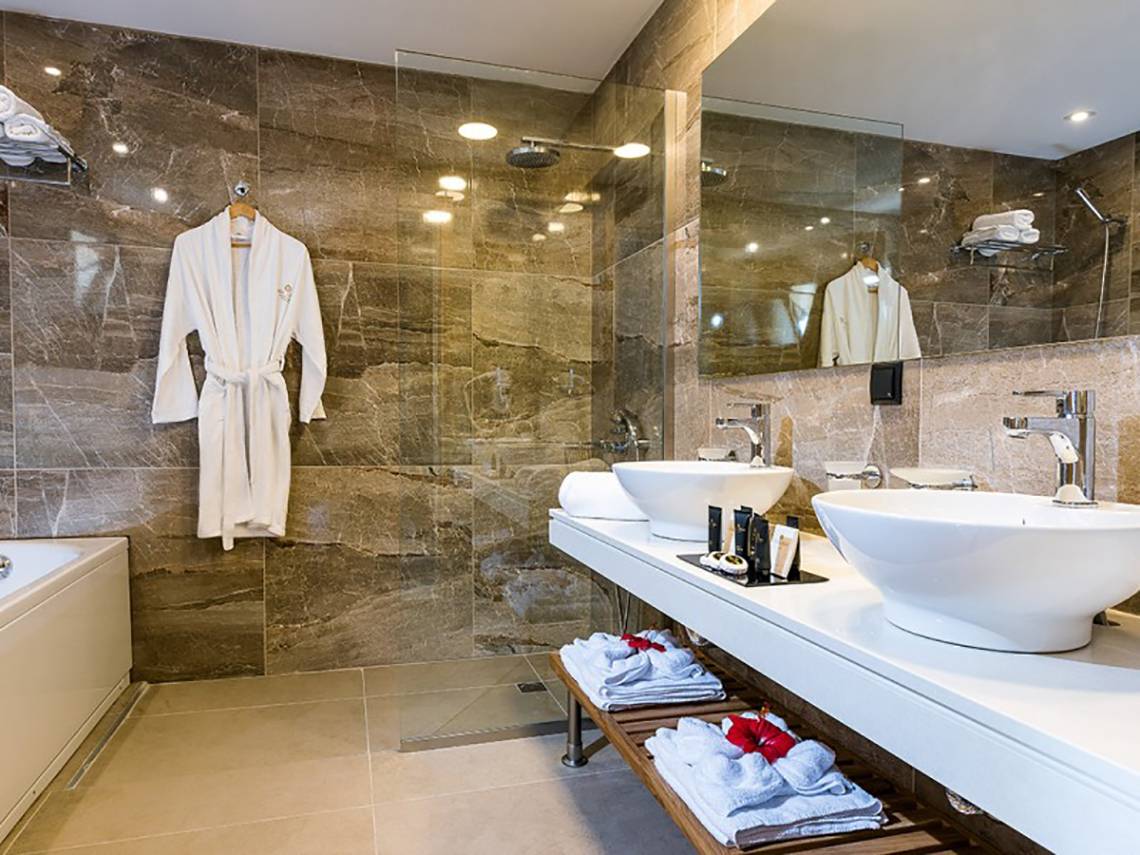 Ein elegantes Badezimmer im Stella Palace Resort & Spa mit Marmorwänden, zwei Waschbecken und einer Badewanne.
