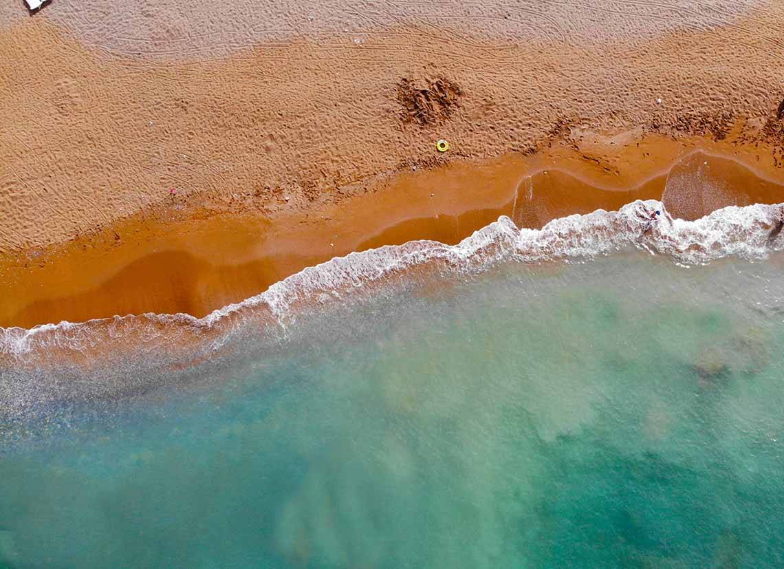 Luftaufnahme des Eftalia Holiday Village Strands und Meeres mit braunem Sand und blauem Wasser