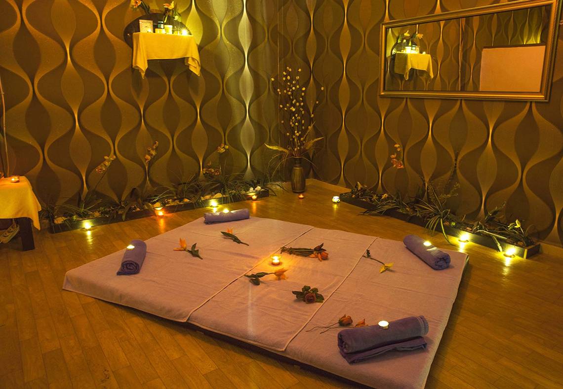 Massagebereich im Eftalia Holiday Village mit Kerzen, Blumen und gerollten Handtüchern auf einem violetten Tisch.