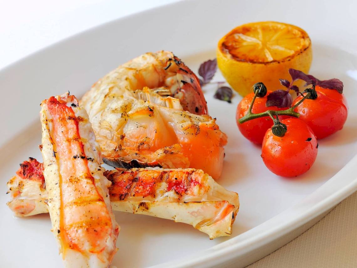Gegrillte Garnelen und Krebse auf einem weißen Teller mit Zitrone und Tomaten