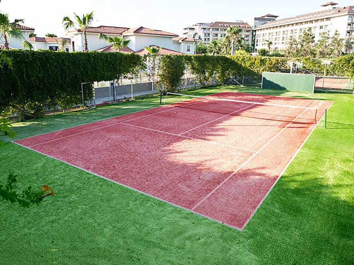 Tennisplatz des Paloma Oceana Hotels mit rotem Hartplatz und umlaufendem Rasen.
