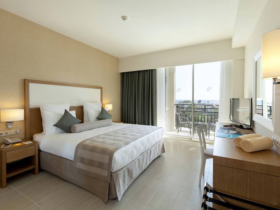 Innenansicht eines eleganten Hotelzimmers im Paloma Oceana Hotel mit großem Bett, Balkon und Meerblick.