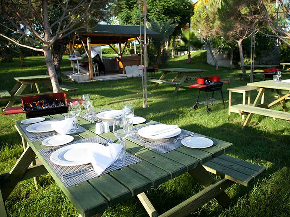 Grillbereich im Garten des Paloma Oceana Hotels mit gedeckten Tischen und Bänken.