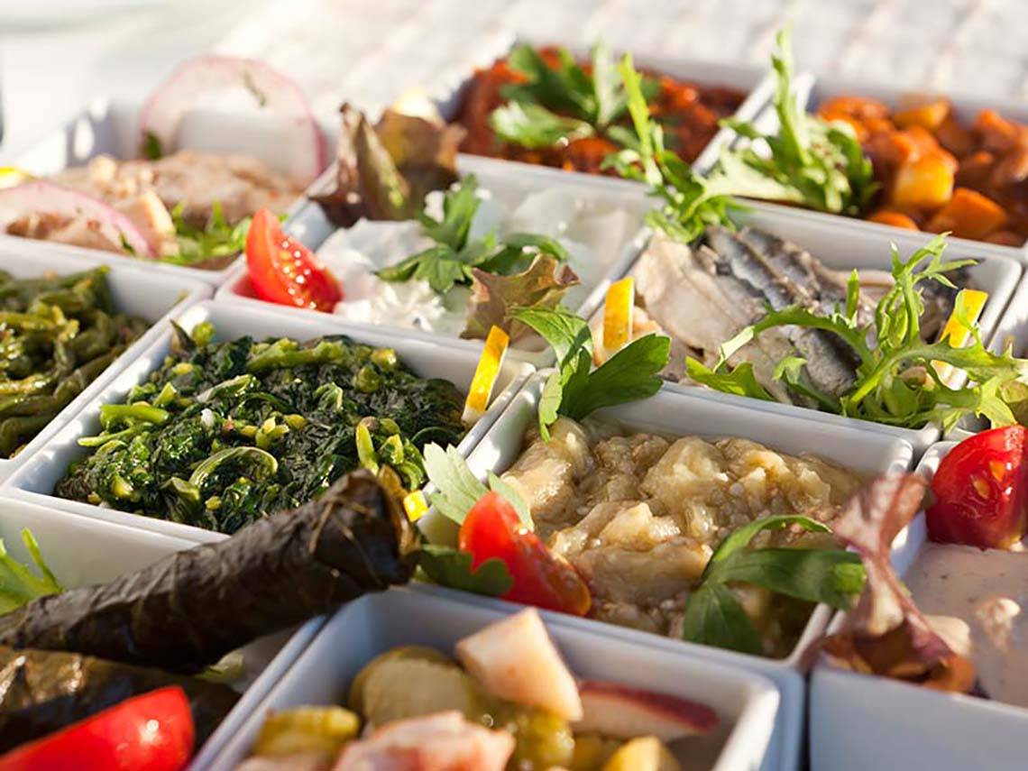 Verschiedene Gerichte auf einem gefütterten Tablett serviert, einschließlich Tomaten, grünem Gemüse, Fisch und anderen Zutaten.