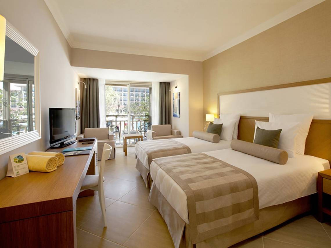 Doppelzimmer im Paloma Oceana Hotel mit zwei Betten, Fernseher, Schreibtisch und Balkon.