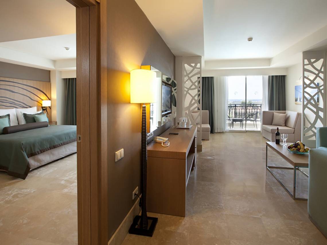 Innenansicht eines Paloma Oceana Hotelzimmers mit Bett, Wohnzimmer und Balkon