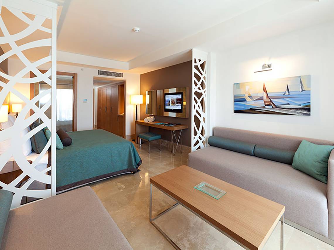 Interieur eines Hotelzimmers im Paloma Oceana Hotel mit einem Bett, Sofa, Tisch und Fernseher.