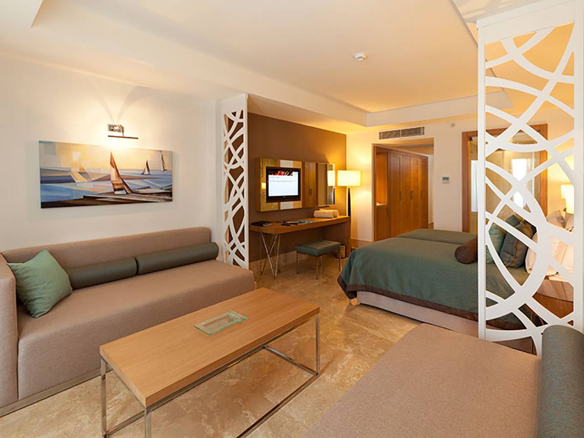 Innenansicht einer Suite im Paloma Oceana Hotel mit Wohnzimmer und Schlafzimmerbereich.