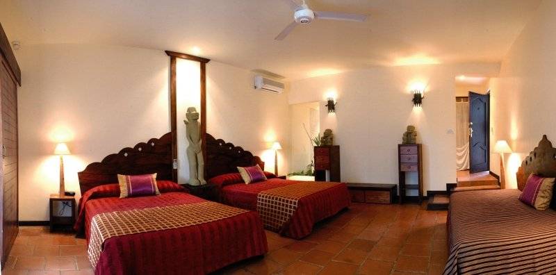 Schlafzimmer im Jardin del Eden Boutique Hotel mit drei Betten, Holzbettrahmen und dekorativen Elementen.