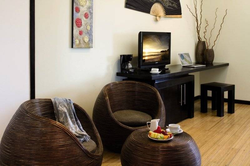 Wohnzimmer mit zwei Korbsesseln, Tisch, Fernseher und Stuhl im Jardin del Eden Boutique Hotel.