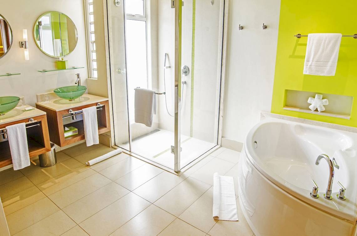 Badezimmer im Tamassa Bel Ombre Hotel mit zwei grünen Waschbecken, einer Duschkabine und einer Badewanne.