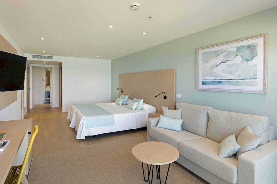 Innenansicht eines Zimmers im HSM Golden Playa Hotel mit Doppelbett, Sofa, Schreibtisch und Fernseher.